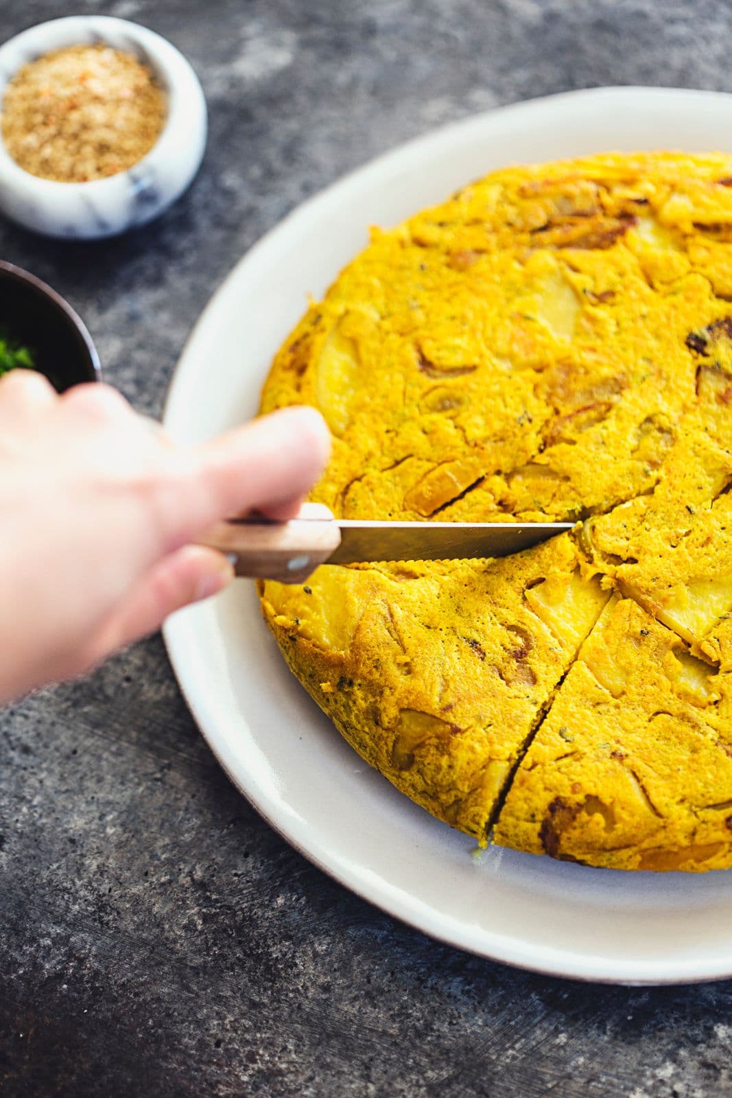 A hand using a knife to slice into the tortilla on a white plate.