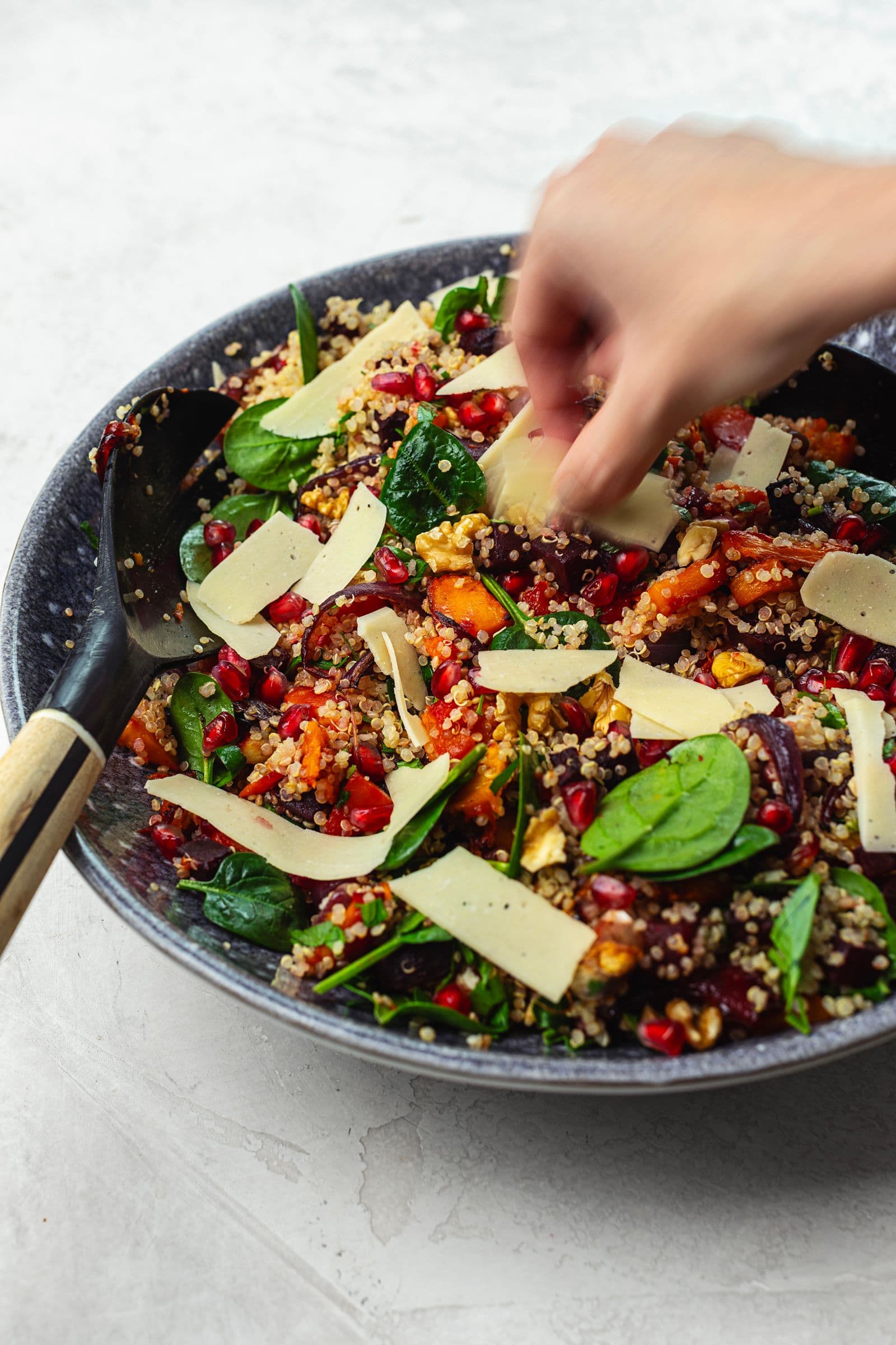 Adding shaved vegan cheese to a quinoa salad with roasted vegetables and pomegranate.