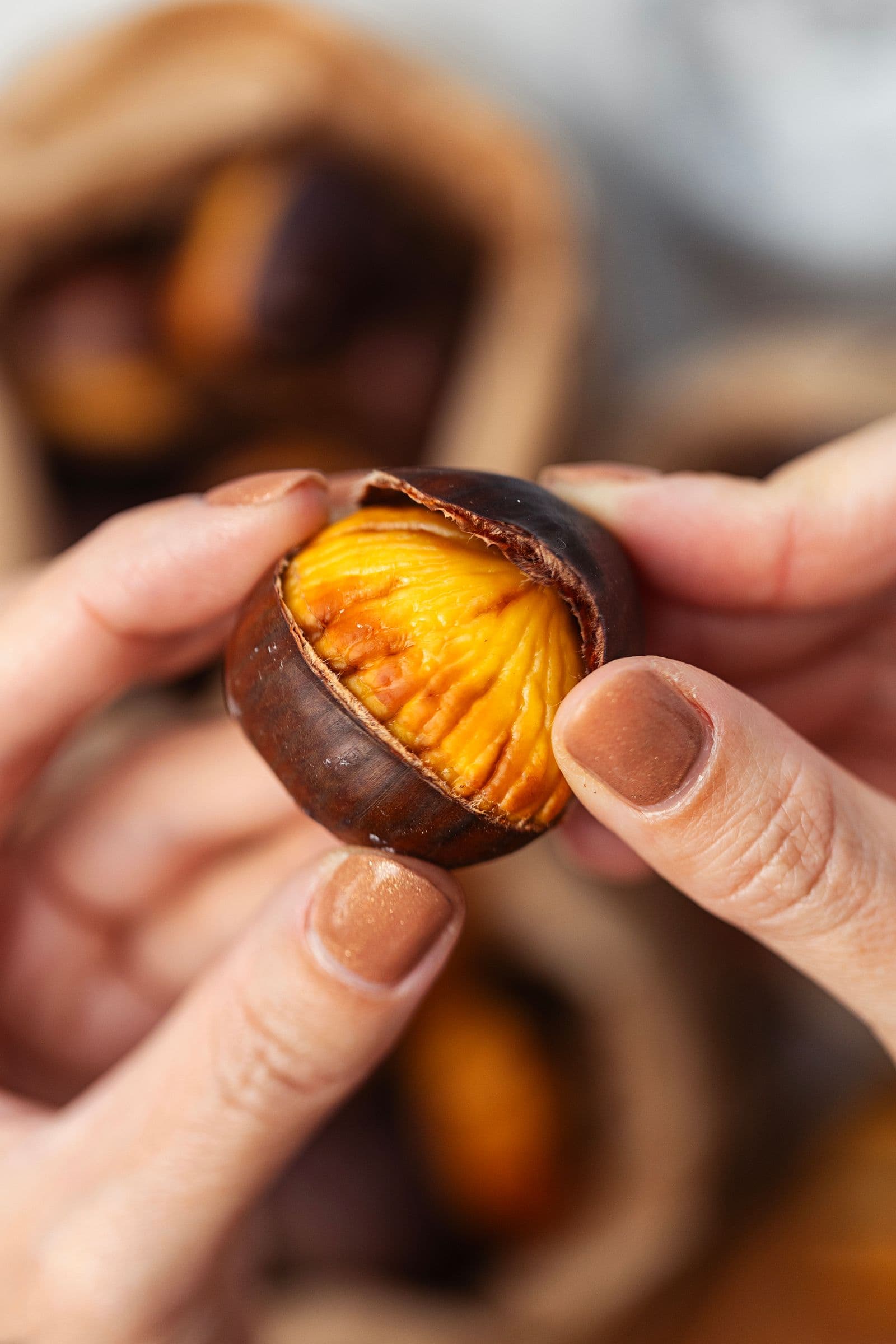 Hands peeling a freshly roasted chestnut, revealing its bright yellow interior.