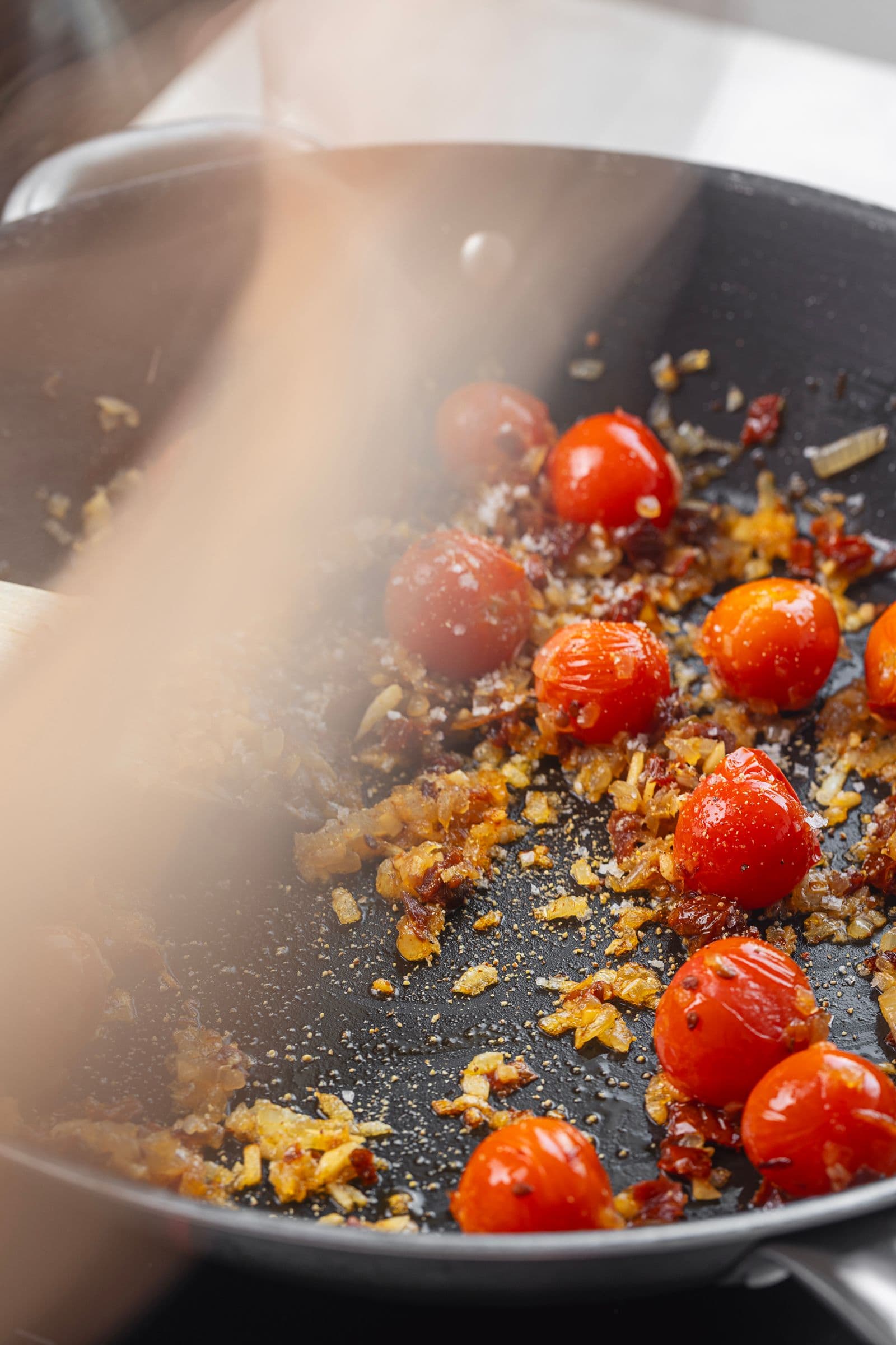 Steaming pan with cherry tomatoes and golden onions cooking together for the risotto base.