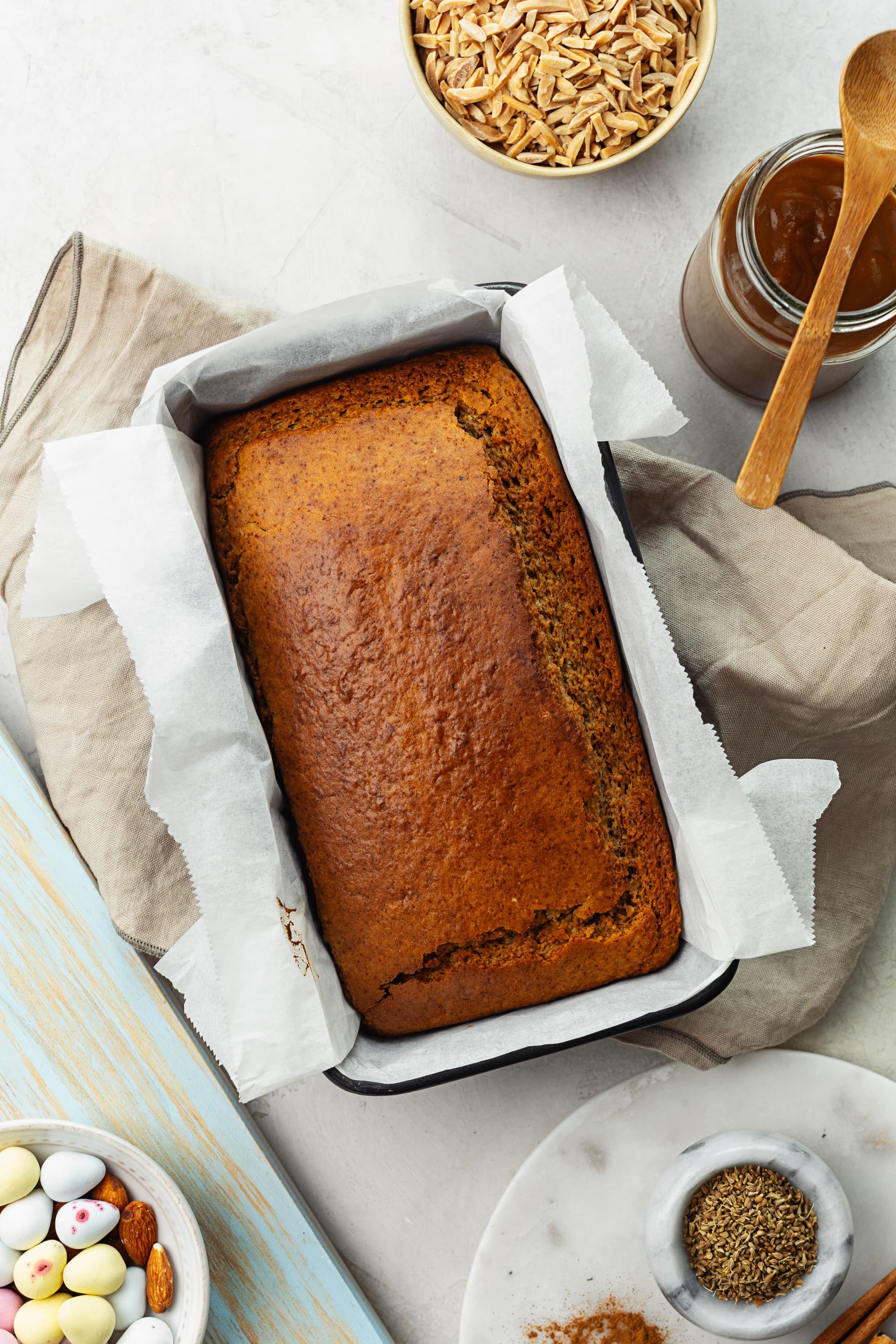 Freshly baked almond cake in the tin with a deep golden crust, surrounded by coconut caramel and spices.