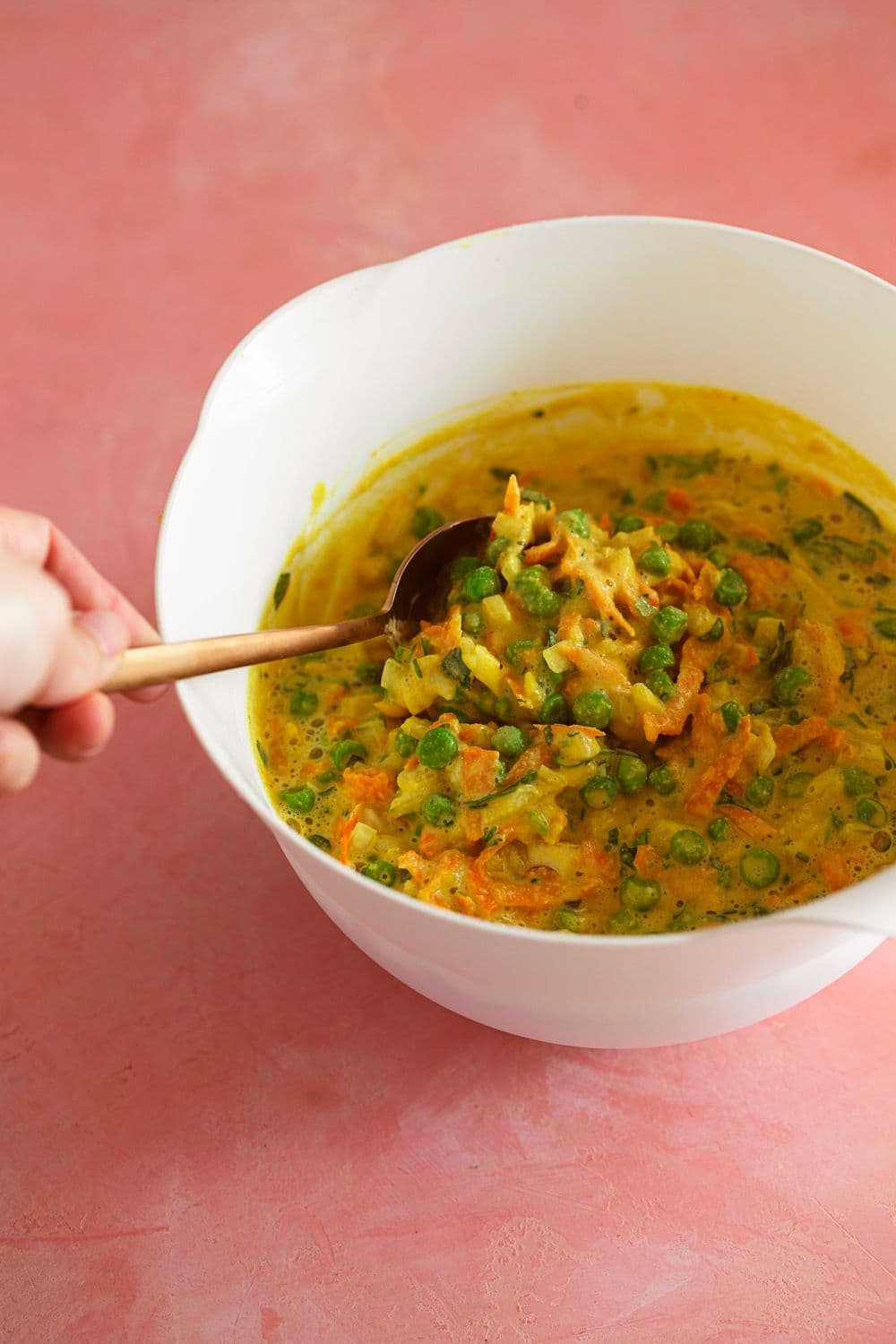 Chickpea fritter batter with shredded carrots and peas in a white mixing bowl