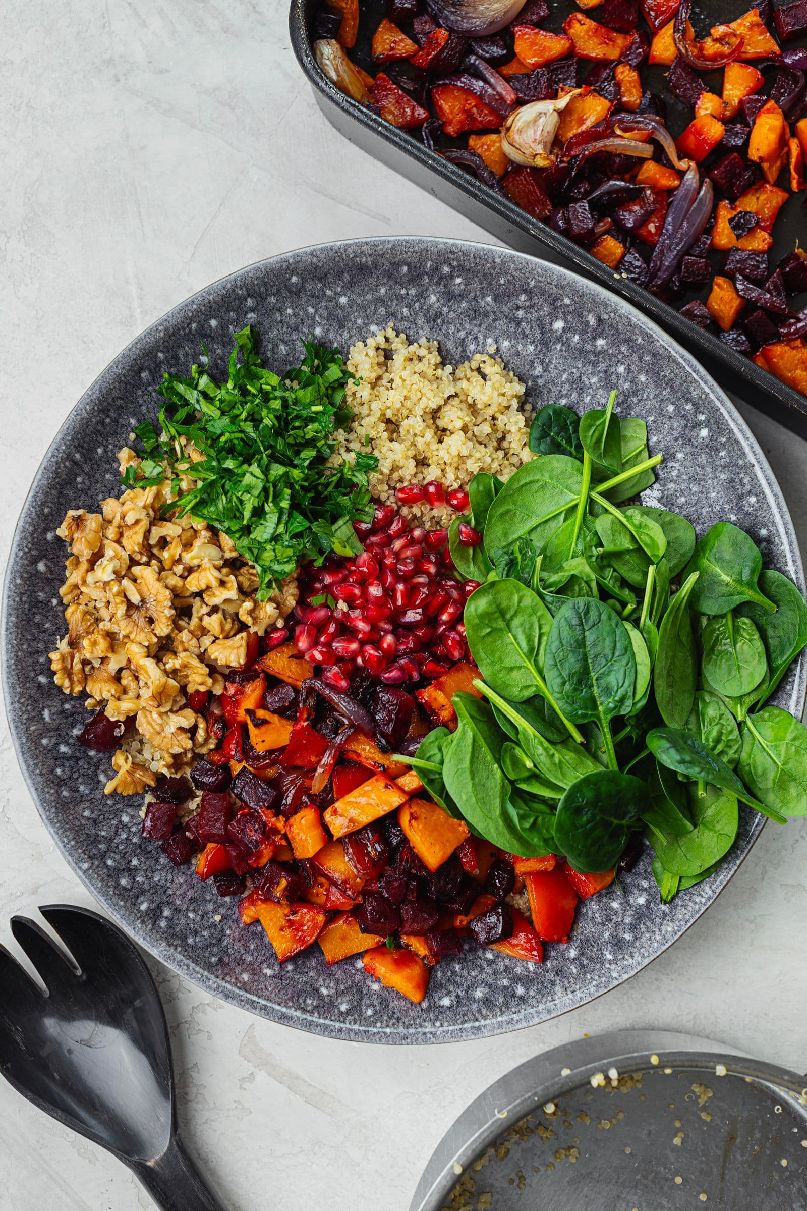 Salada de inverno em preparação, com quinoa, vegetais assados, espinafres, nozes, romã e ervas frescas.