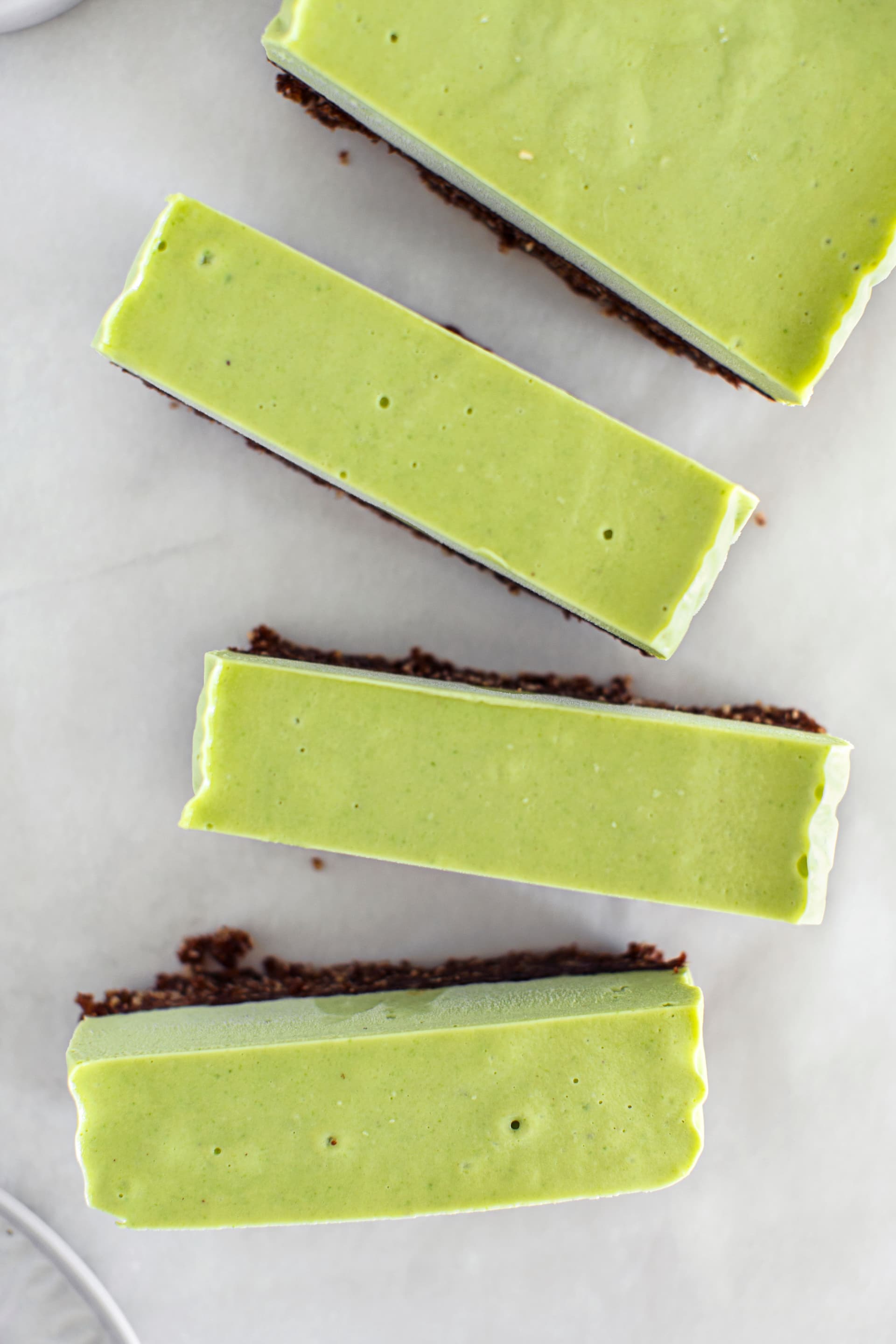 Rectangular slices of vegan mint cheesecake on a chocolate base, arranged on a light background.