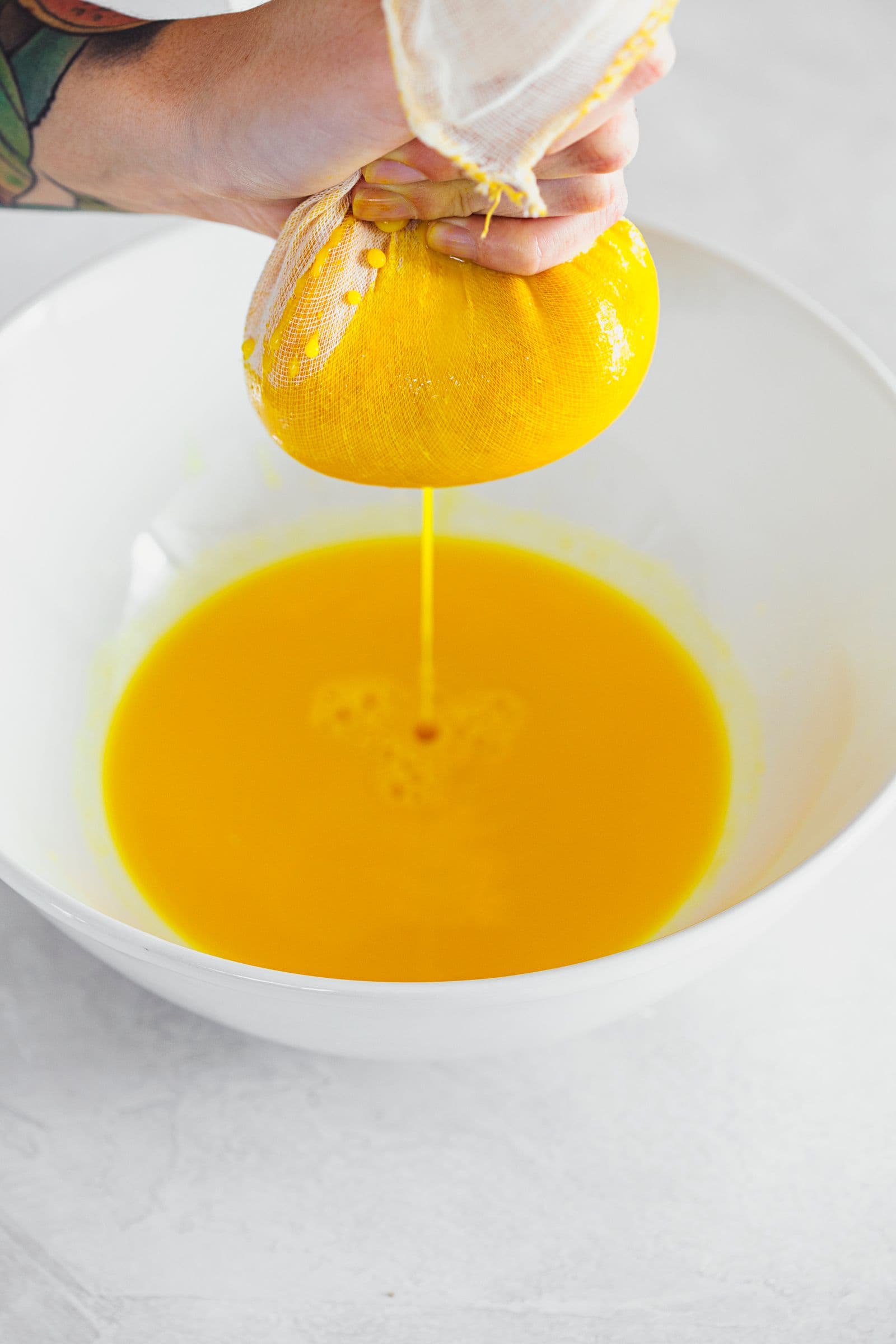 Hand squeezing bright orange syrup concentrate from cloth into a bowl.