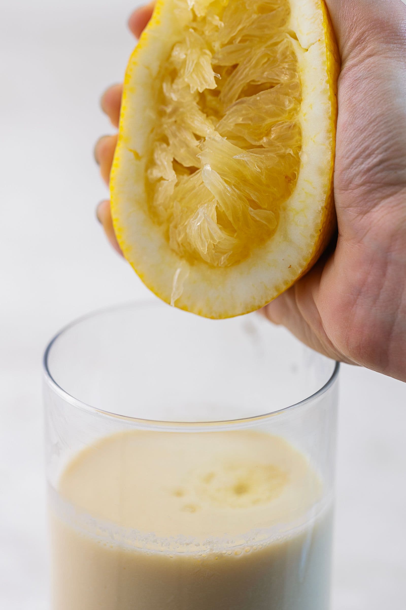 Hand squeezing a lemon half over a glass of soy milk to make vegan buttermilk for pancakes