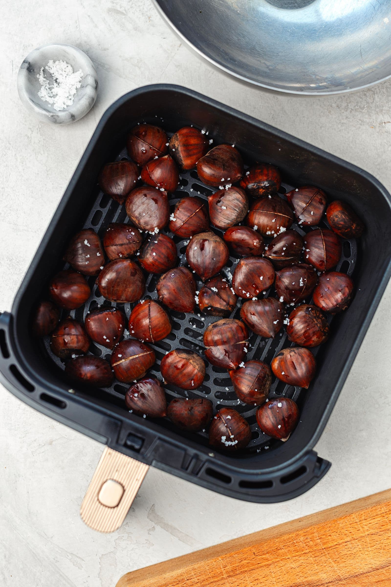 Drained chestnuts sprinkled with coarse salt inside the air fryer basket before roasting.