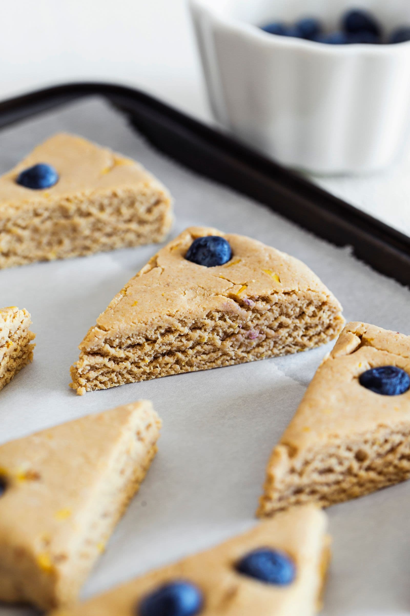 Raw vegan lemon and blueberry scones spaced out on parchment paper before baking.