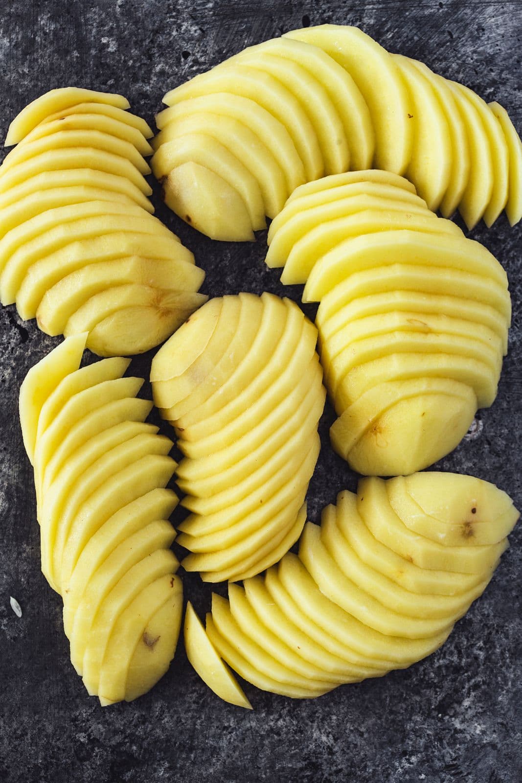 Thinly sliced potatoes arranged in neat rows on a dark surface.