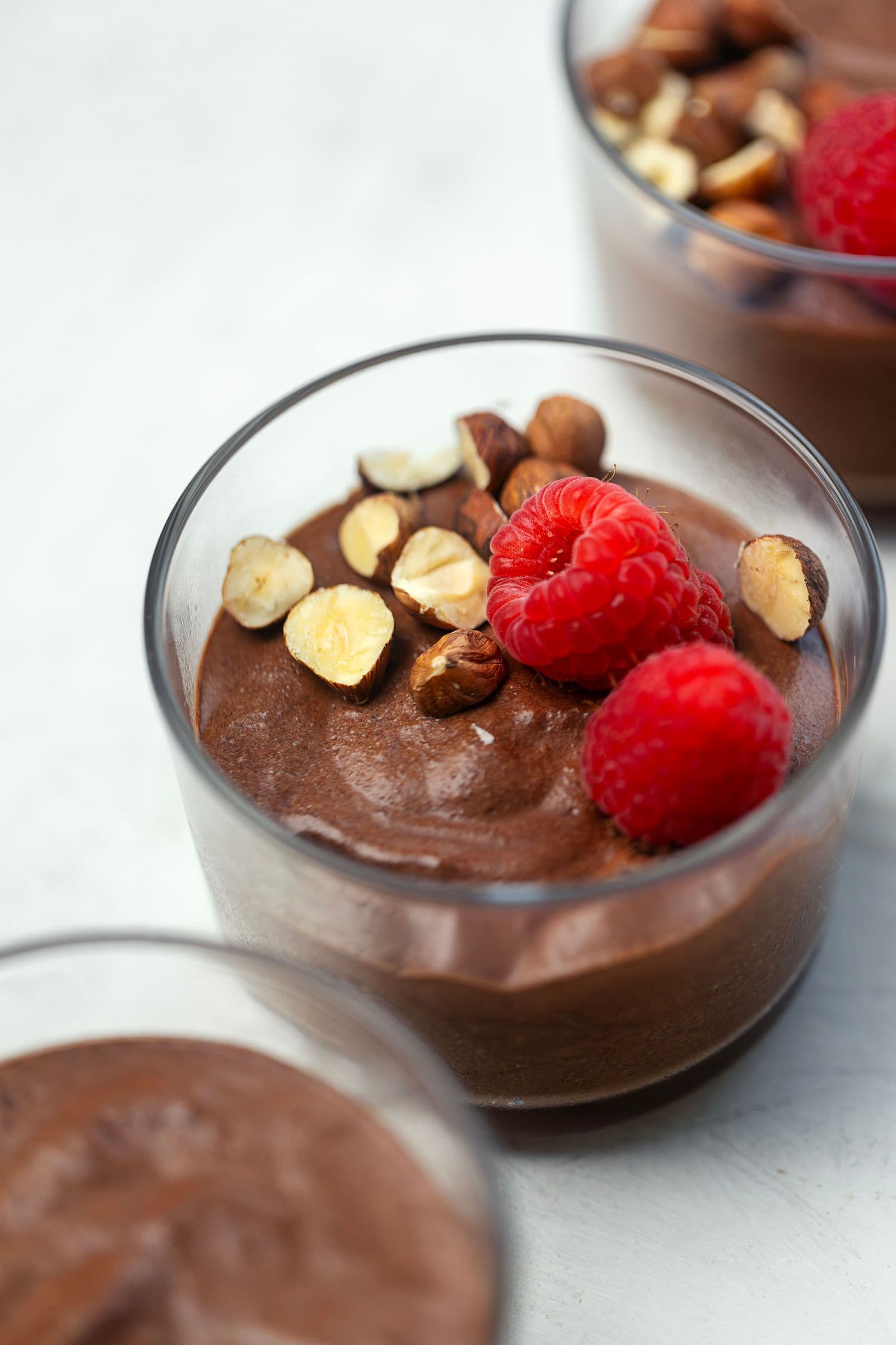 Close-up of vegan chocolate mousse in a glass cup topped with raspberries and nuts.