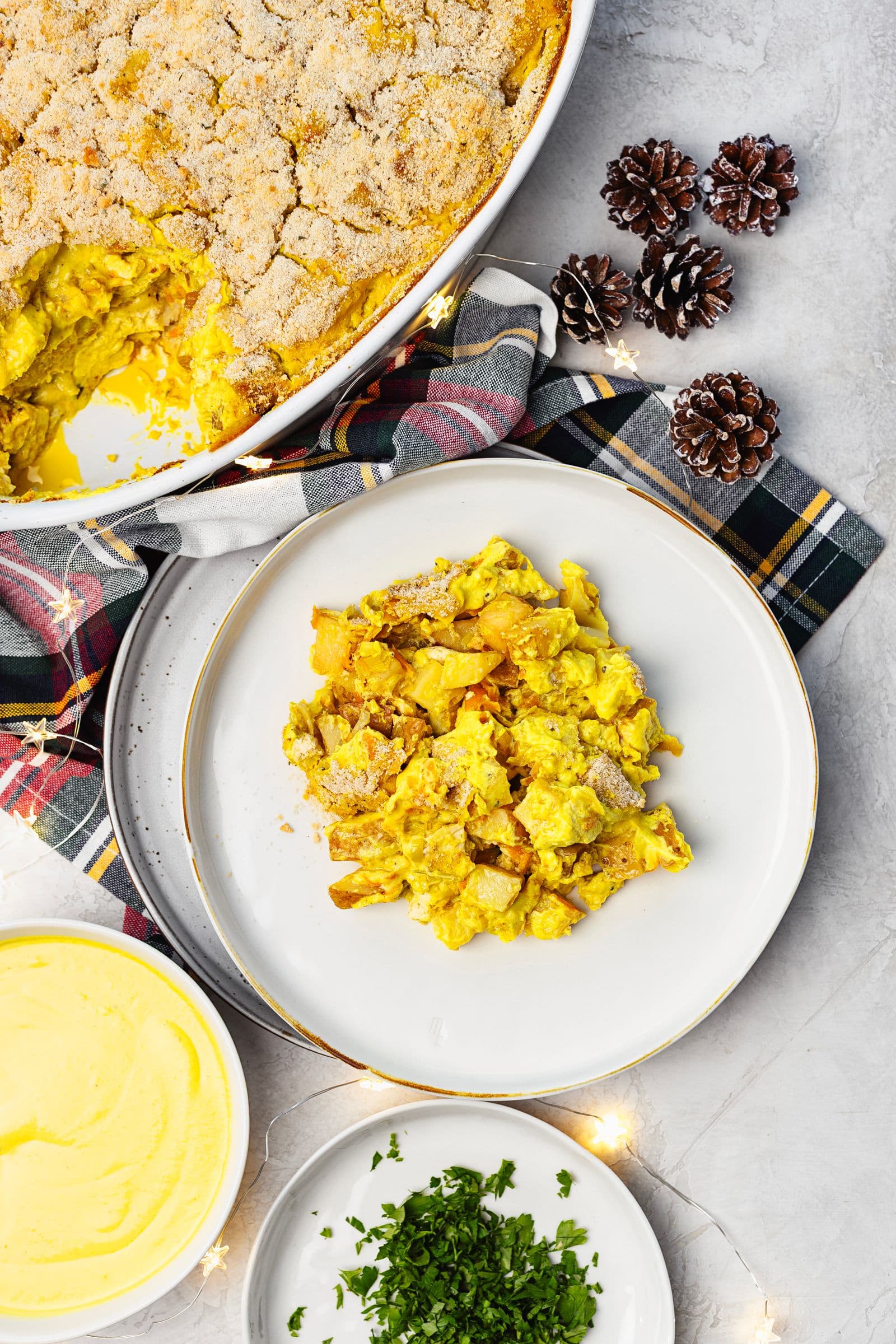 Gratin dish with a serving on a plate, accompanied by fresh parsley and extra sauce.