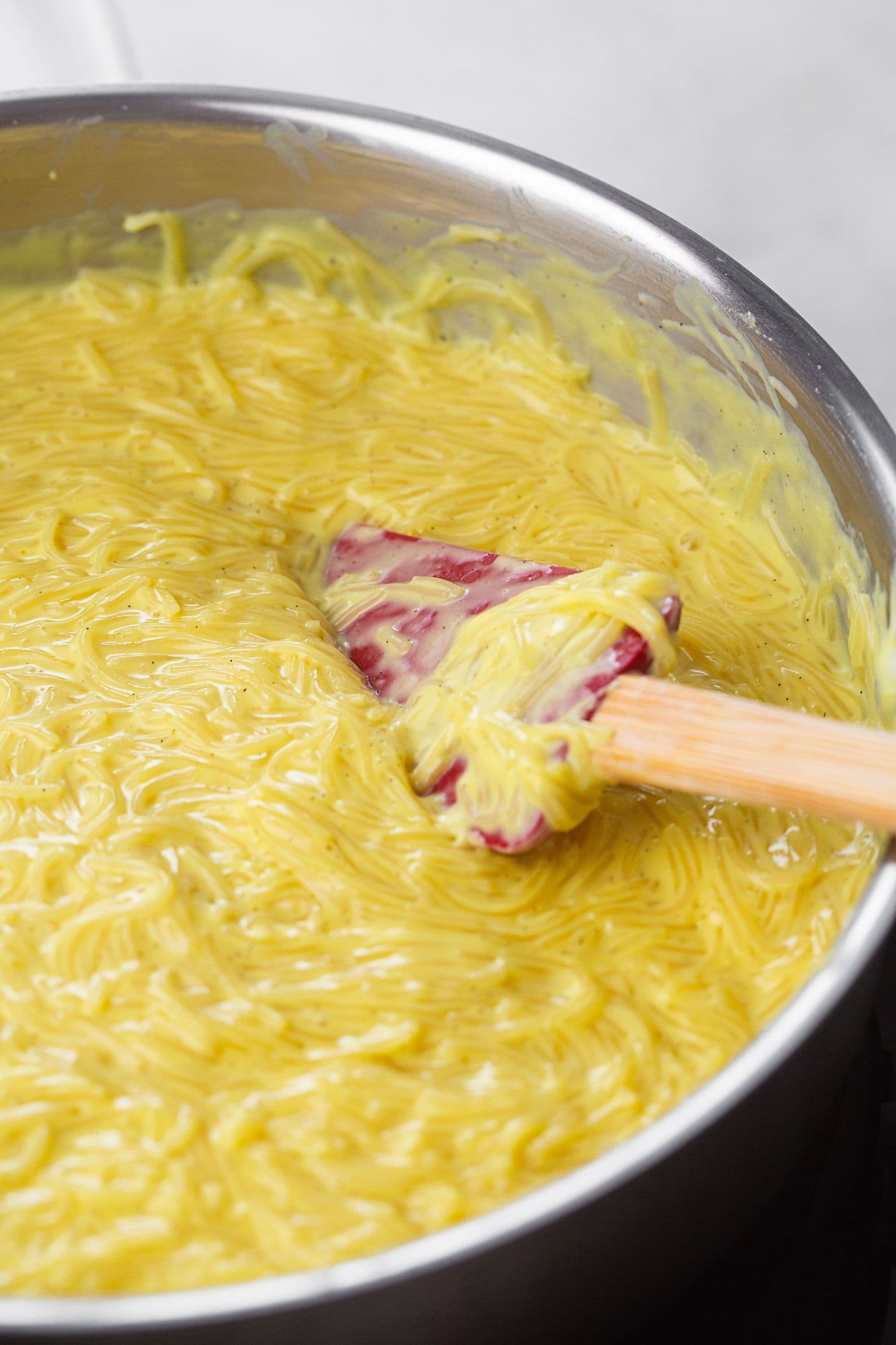 Close-up of vegan Aletria cooking in a saucepan, with a spatula stirring the creamy, golden mixture.