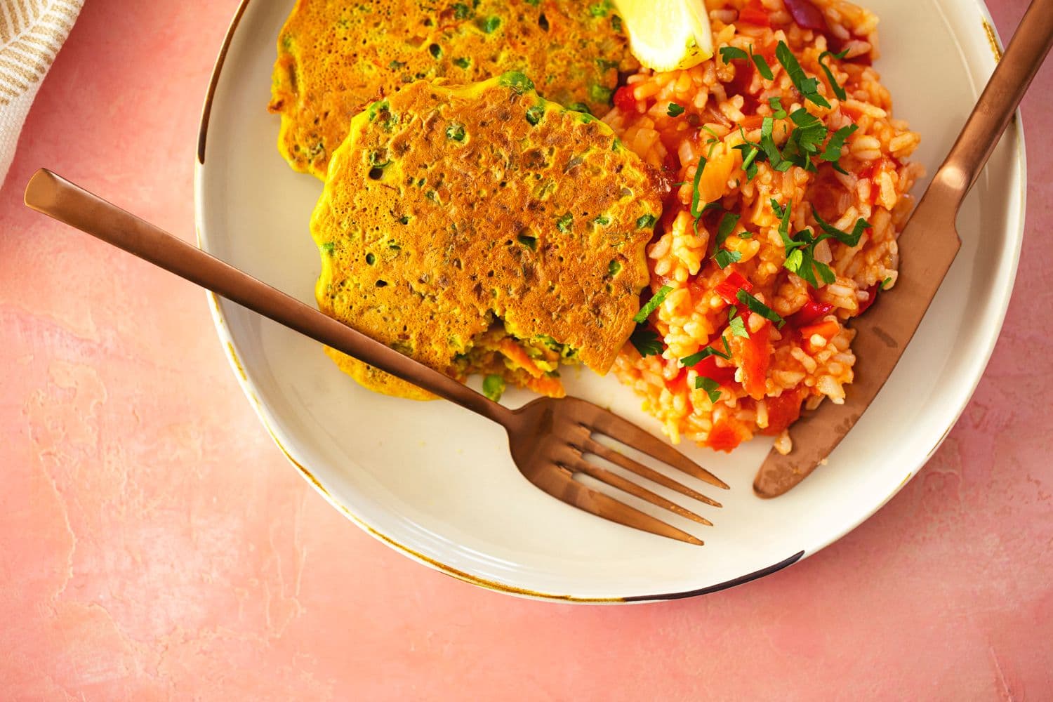 Colourful vegan meal with fritters and tomato rice, served with gold cutlery