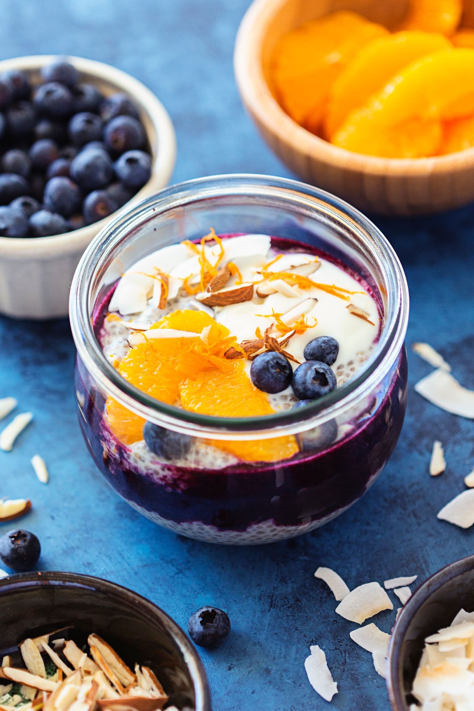 Glass jar of chia pudding layered with blueberry purée, fresh orange slices and coconut flakes.
