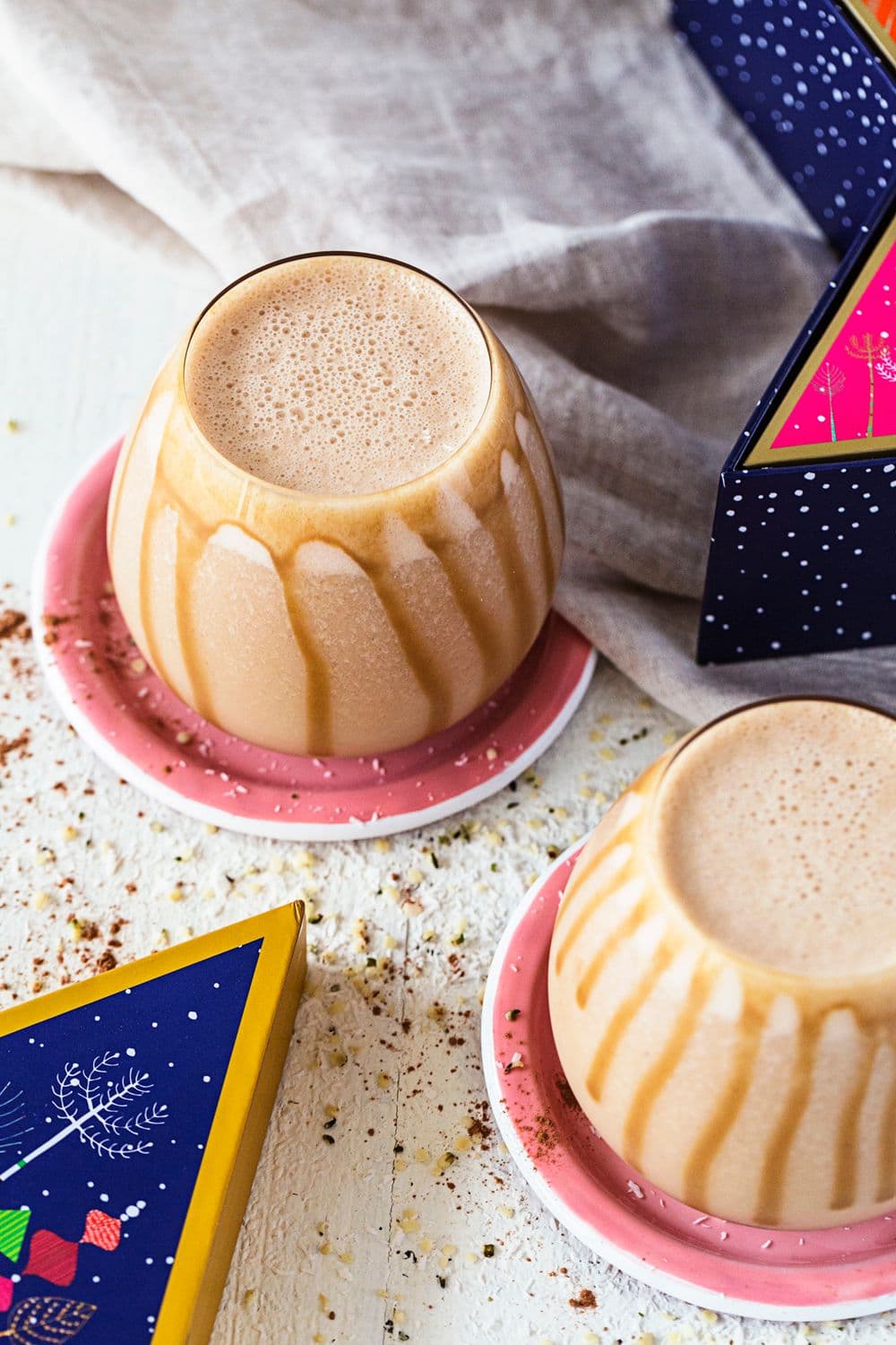 Rounded glasses with salted caramel and peanut butter smoothie, drizzled with caramel sauce, on pink coasters.