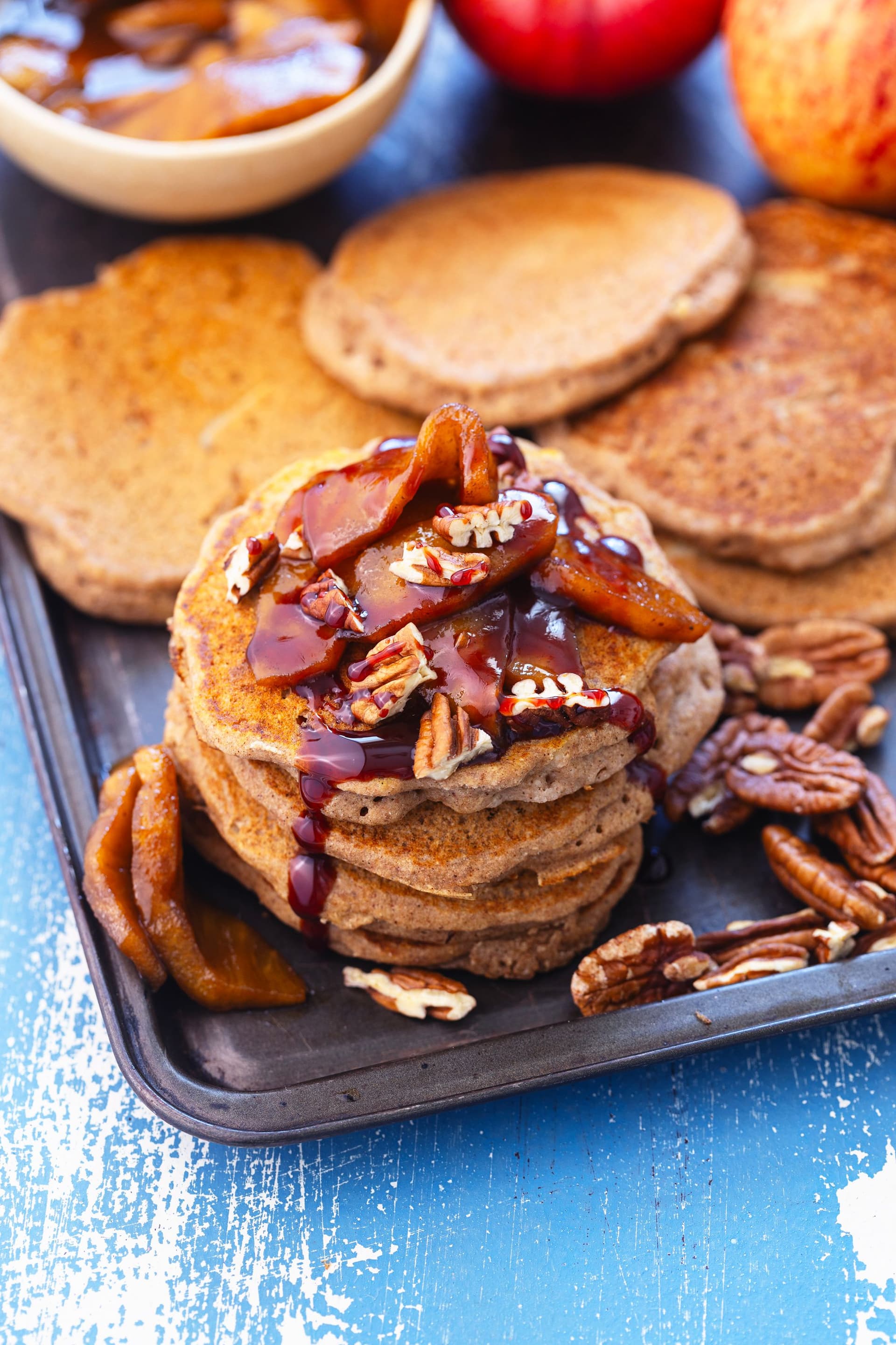 Stack of apple buckwheat pancakes topped with coconut caramel apples, pecans and syrup.