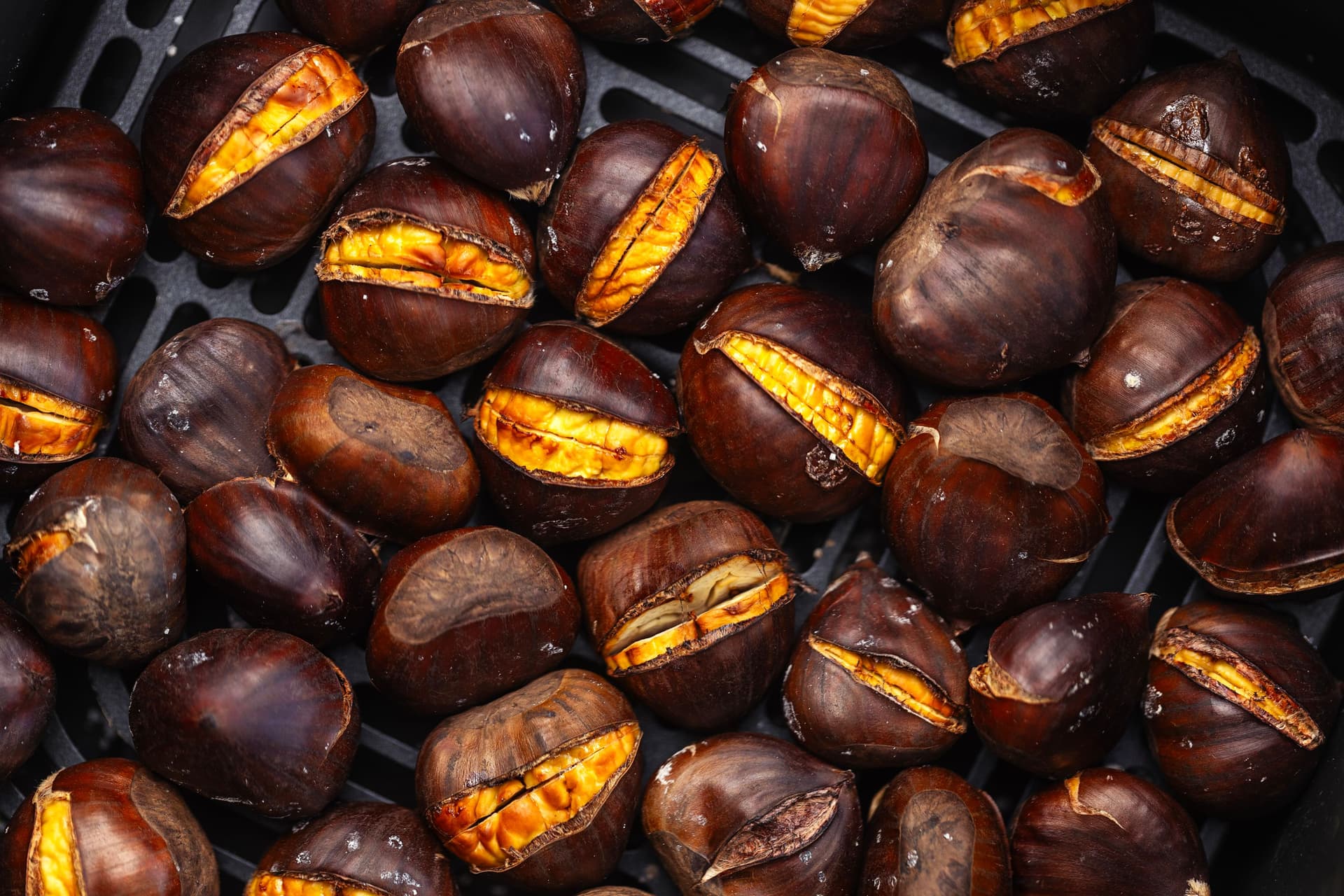 “Close-up of roasted chestnuts inside the air fryer, showing the bright yellow flesh peeking through the opened shells.”