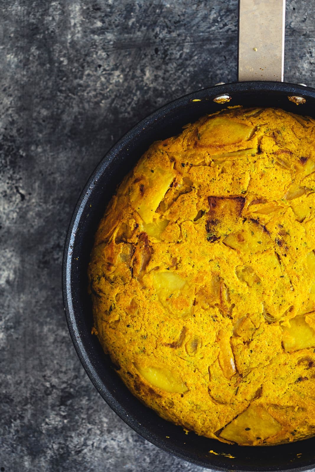 Cooked vegan tortilla in a black skillet, golden on top and ready to slice.