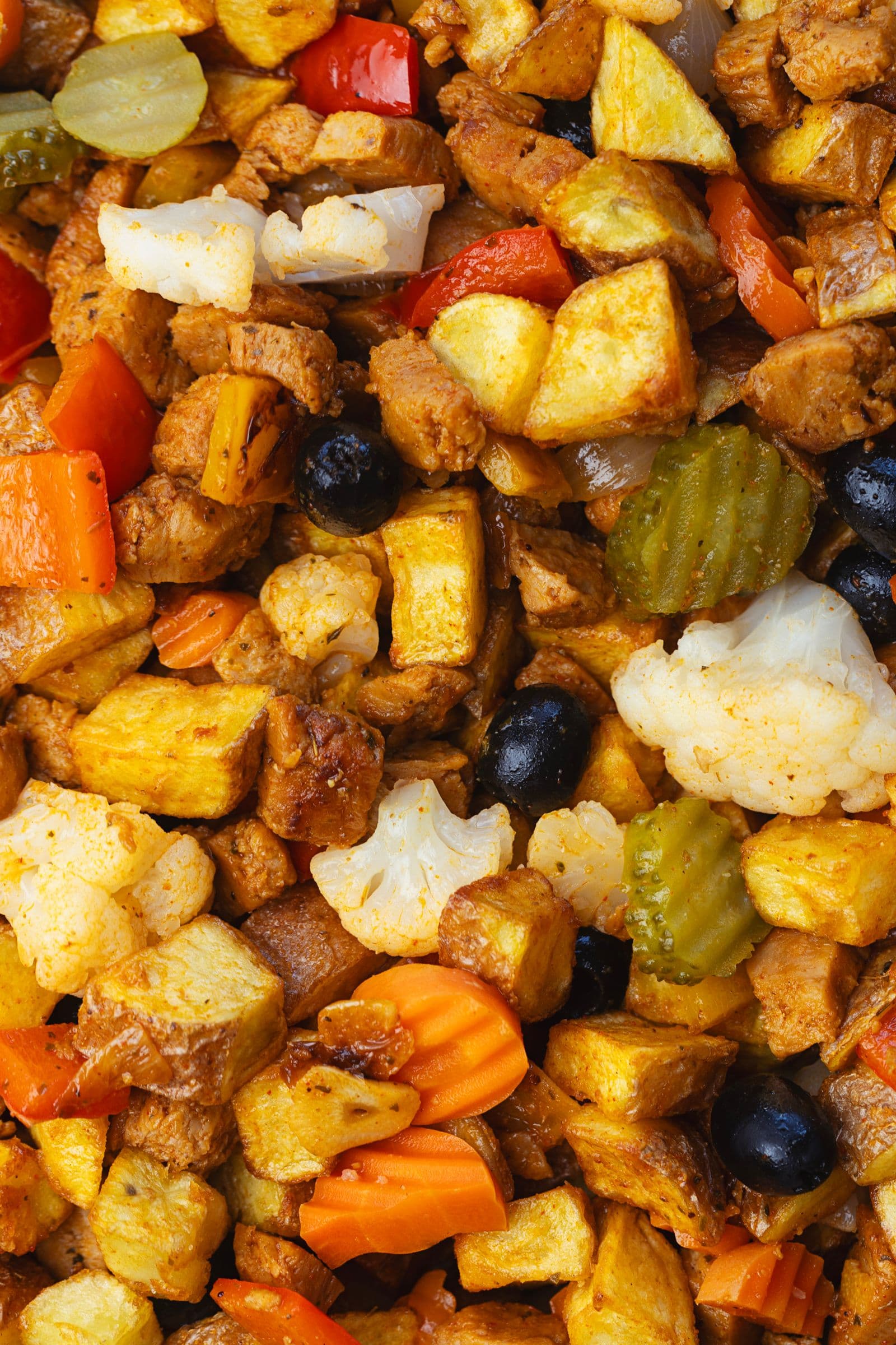 Close-up of soy pica pau with crispy potatoes, black olives, pickled cauliflower and carrots, caramelised soy chunks and bell peppers