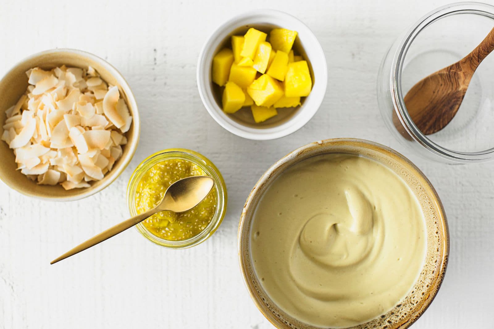 Small bowls with toasted coconut, fresh mango chunks, mango chia jam and creamy mango cashew yogurt.